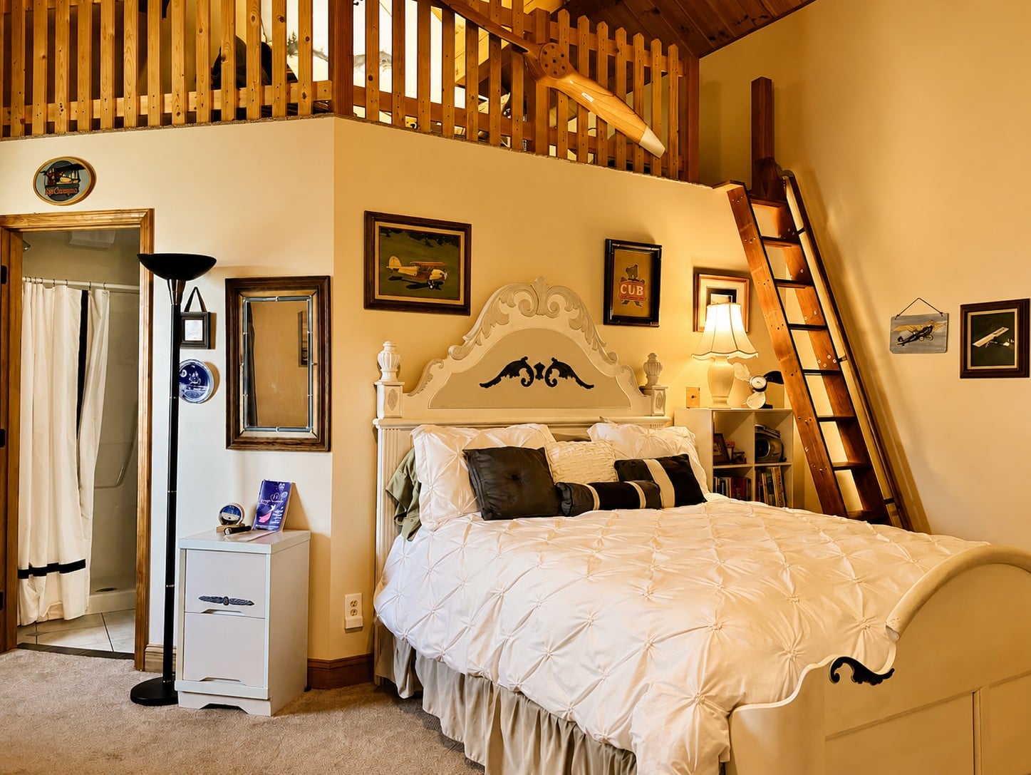 Aviation-themed loft guest room at Bedford Landings Bed & Breakfast near Smith Mountain Lake, featuring a cozy white bed, wood-paneled loft, ladder, private bathroom, and warm cabin-style decor.