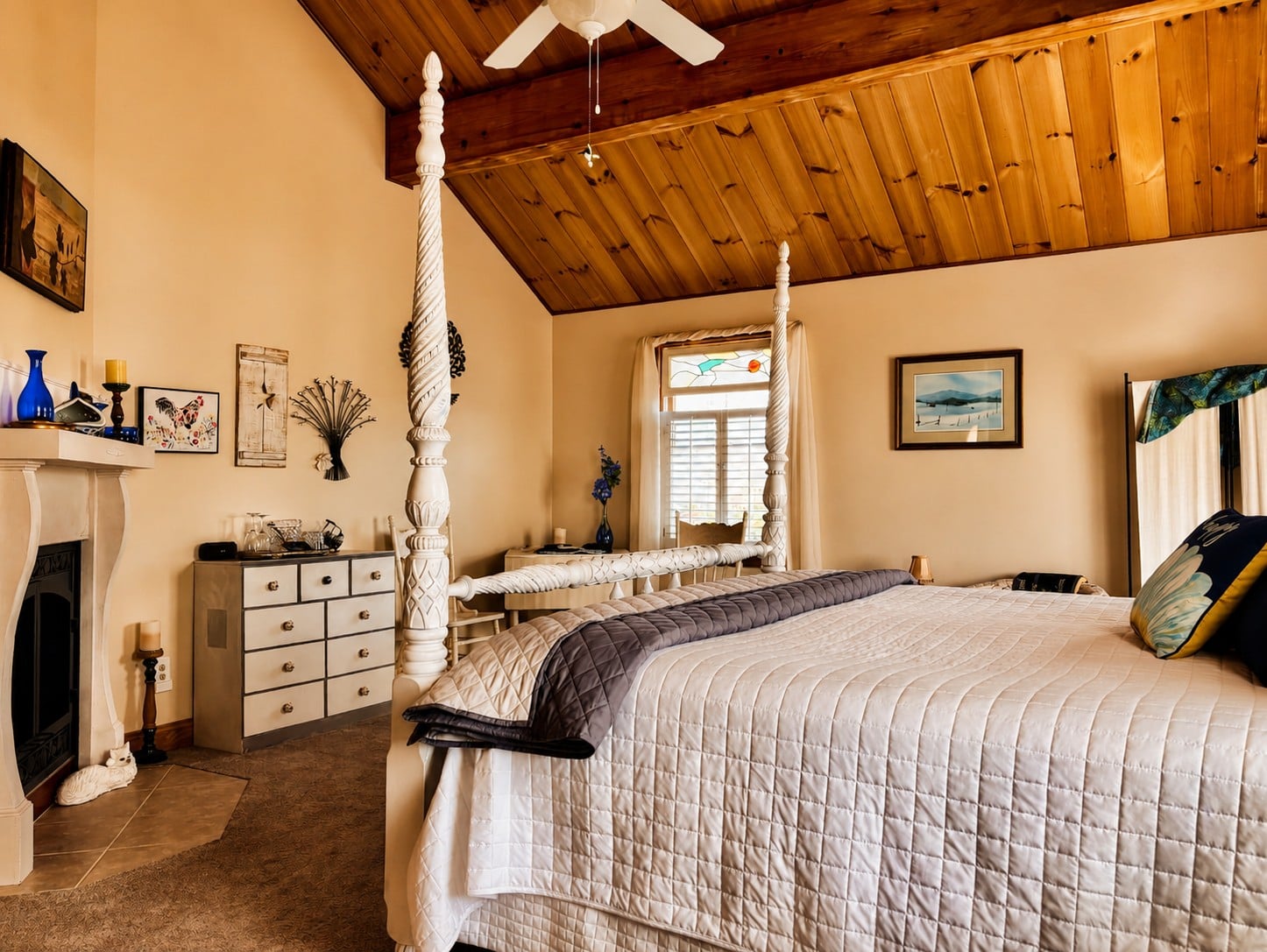 Guest room at Bedford Landings Bed & Breakfast near Smith Mountain Lake, featuring a white four-poster bed, vaulted wood ceiling, cozy fireplace, stained-glass window, and warm natural light.