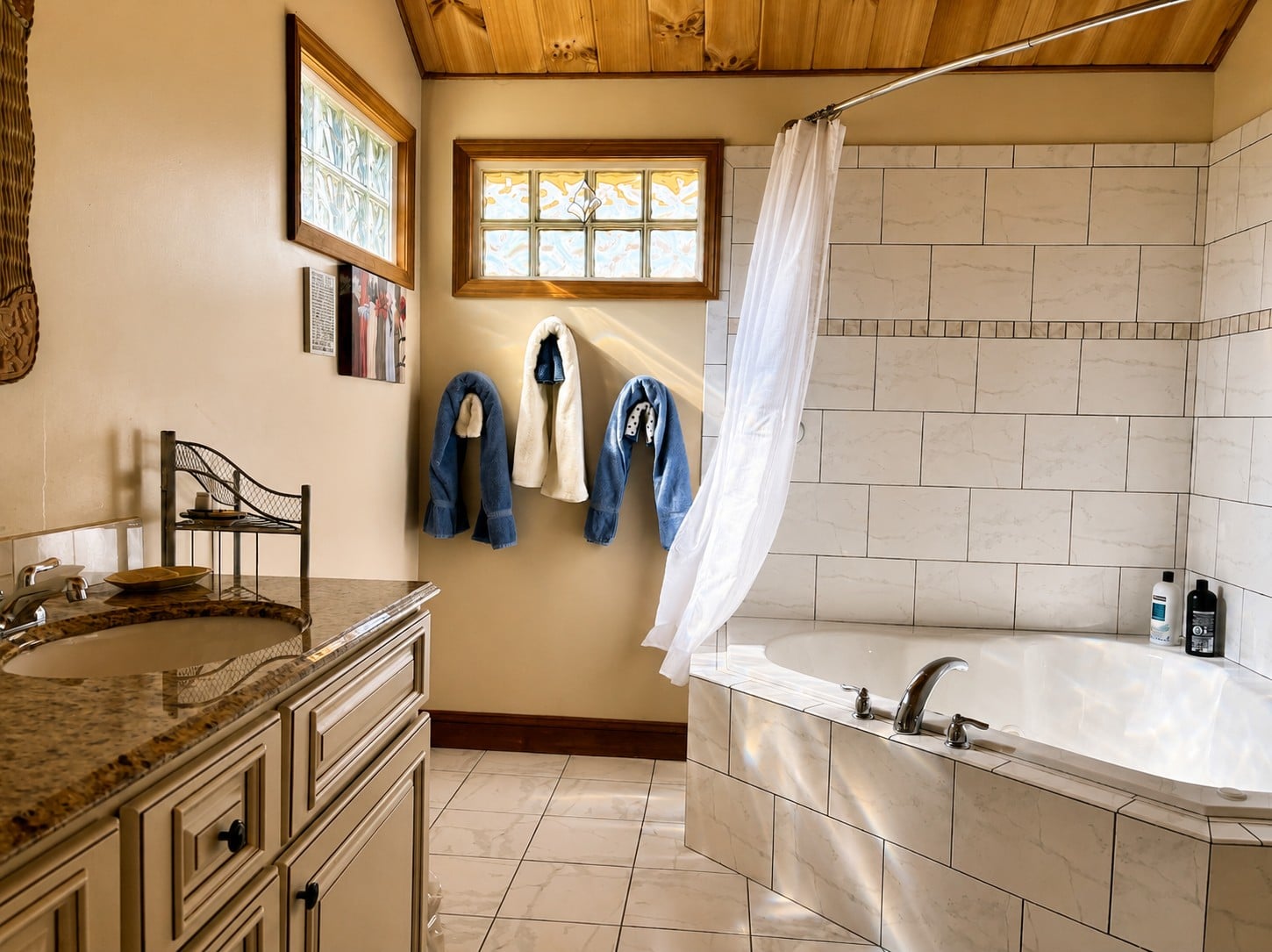 Guest bathroom at Bedford Landings Bed & Breakfast near Smith Mountain Lake, featuring a jetted tub, tiled shower surround, rustic wood ceiling, warm natural light, and cozy bathrobes.